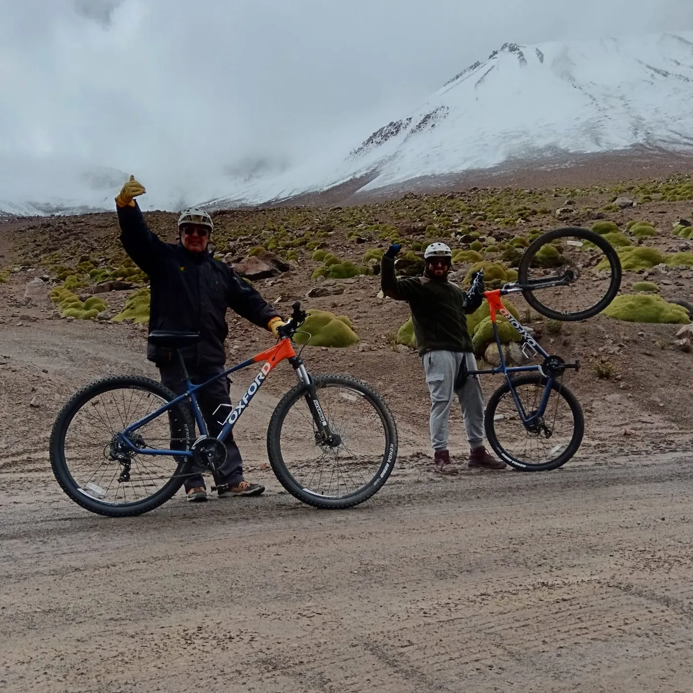 Ciclistas celebrando con las bicicletas en alto frente al volcán nevado
